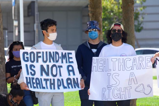 A guy holding a sign that reads "Go Fund Me is not a Healthcare Plan"