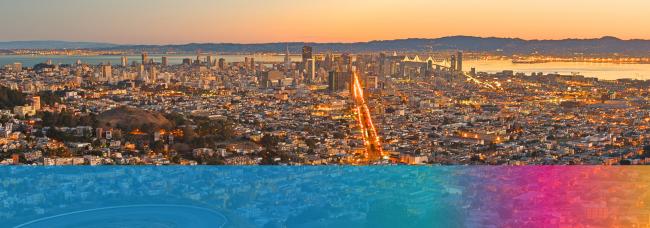 A birds eye view of San Francisco at sunset. A brightly-lit Market Street cuts across the city. A blue, then purple-yellow gradient streak stretches across the bottom of the image.